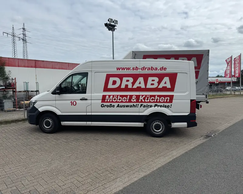 Weißer DRABA Transporter mit Schriftzug Möbel und Küchen auf Parkplatz vor Fahnen